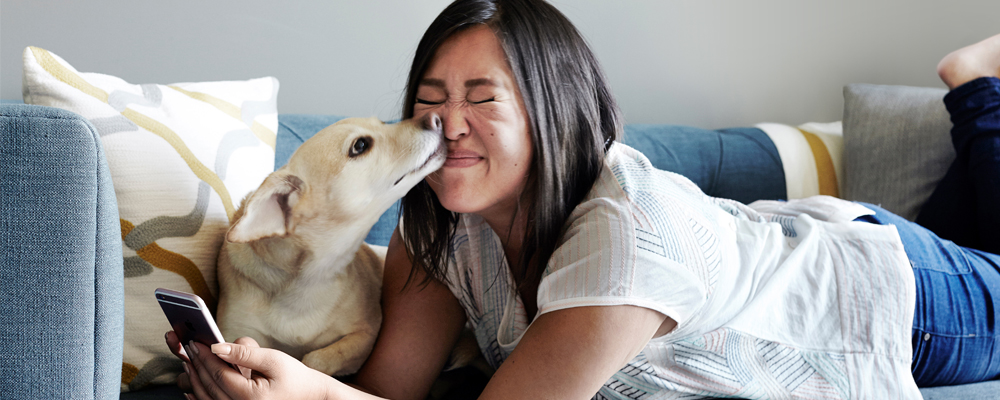 Woman on the couch with her dog licking her face